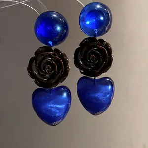 Vue détaillée de boucles d'oreilles en résine bleue avec rose sombre et cœur suspendu