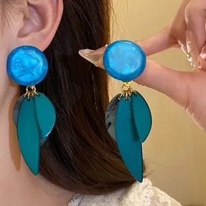 Gros plan de grandes boucles d'oreilles en résine bleue avec des feuilles marbrées.
