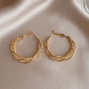 Detailed macro shot of elegant golden twisted mesh hoop earrings on silk background