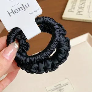Close-up detail of black silk-like ruffled hair scrunchies showing elegant fabric texture