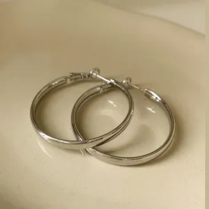 Macro view of minimalist silver geometric hoop earrings on a smooth ceramic surface