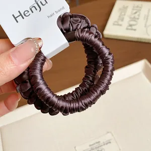 Close-up detail of a coffee brown pleated fabric scrunchie with elastic hair tie.