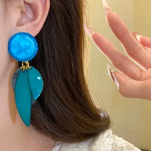 Détail de grandes boucles d'oreilles en résine bleue avec un motif de feuilles élégant