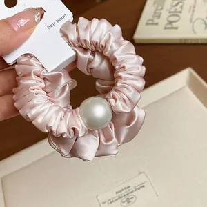 Close-up view of a pink satin pleated scrunchie featuring a large elegant pearl detail.