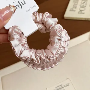 Detailed view of a pink pleated satin scrunchie highlighting the soft fabric texture