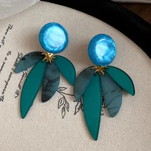 Détail de boucles d'oreilles en résine bleue et pendentifs feuilles sur tissu texturé
