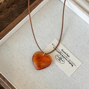 Macro view of heart-shaped amber resin pendant necklace with brown cord on fabric background
