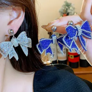 Detailed macro view of sparkling rhinestone-encrusted resin bow earrings in silver and blue.
