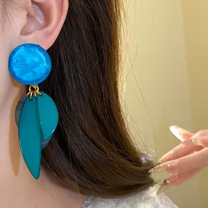 Détail de boucles d'oreilles en résine avec clou bleu et pendentifs feuilles bleu sarcelle