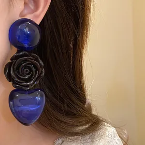 Gros plan détaillé des boucles d'oreilles cœur en résine bleue et rose noire sur modèle