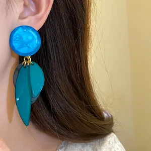 Gros plan détaillé montrant une boucle d'oreille en résine bleue avec pendentifs feuilles