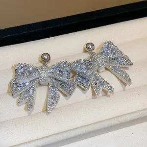Detailed macro view of silver needle bow earrings encrusted with sparkling rhinestones.