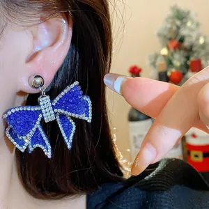 Close-up of a royal blue resin bow earring with sparkling rhinestones for holiday style.