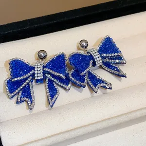 Macro detail of blue resin bow earrings with shimmering rhinestone borders on tray