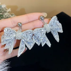 Detailed macro view of silver bow earrings with sparkling rhinestones held by hand