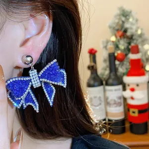 Detail view showing a model wearing elegant sparkling blue resin bow earrings with rhinestones