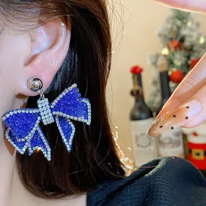 Close-up view of a large blue resin bow earring with sparkling rhinestones worn by a model
