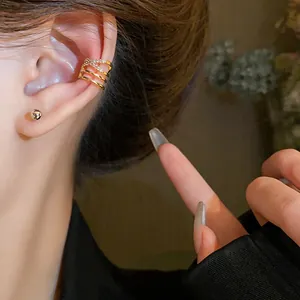 Close-up view of a multi-layer zircon ear cuff and simple gold stud on a model's ear
