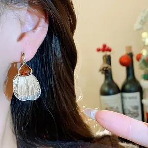 Close-up of retro silver earrings with amber glass and metallic petal tassels worn on ear