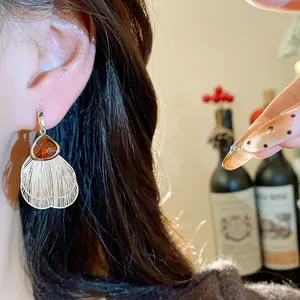 Detailed close-up of silver petal tassel earring with amber glass stone on ear