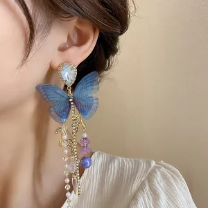 Detailed close-up of an elegant blue mesh butterfly dangle earring with pearls on model