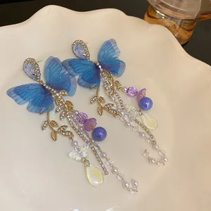 Close-up of elegant blue mesh butterfly earrings with pearl tassels and gold leaves.