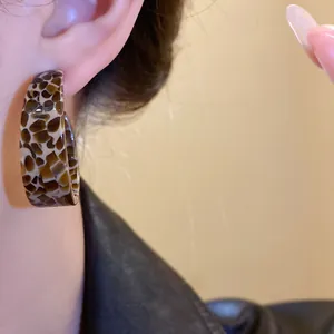 Macro detail shot showing tortoiseshell acetate C-shaped hoop earrings worn on a model's ear