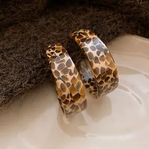 Detailed macro view of retro C-shaped acetate hoop earrings with brown leopard pattern texture