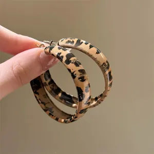Vintage style resin leopard print hoop earrings with silver needles held by hand.