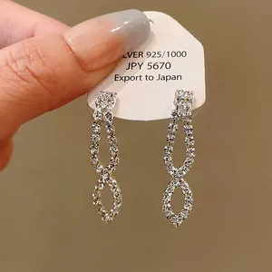 Detail showing silver rhinestone tassel earrings on a display card held by hand.