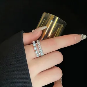 Elegante anello aperto a doppio strato con perle bianche e zirconi lucenti al dito.