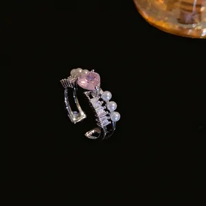 Elegante anello aperto con zircone a cuore rosa e perle su sfondo nero essenziale.