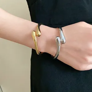 Bracelets joncs ouverts en forme de goutte d'eau or et argent sur le poignet d'un mannequin