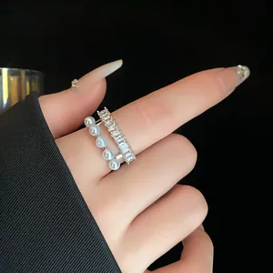 Primo piano di un elegante anello aperto a doppio strato con zirconi e perle indossato al dito.