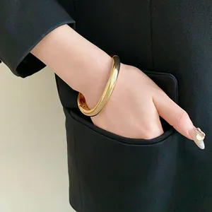 Vue détaillée d'un bracelet jonc en métal doré minimaliste sur un poignet féminin.