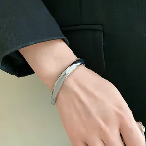 Gros plan d'un bracelet jonc ouvert argenté minimaliste en forme de goutte d'eau au poignet.