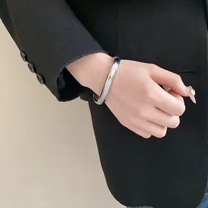 Détail d'un bracelet ouvert en métal argenté minimaliste porté avec un blazer noir