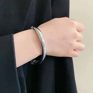 Gros plan d'un bracelet jonc argenté minimaliste élégant porté avec un blazer noir classique