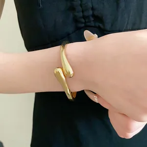 Gros plan d'un bracelet jonc doré en forme de goutte d'eau porté au poignet