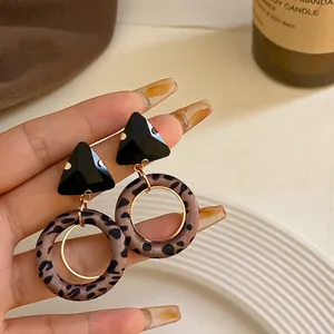 Elegantes pendientes de leopardo con tachuelas geométricas triangulares negras en la mano