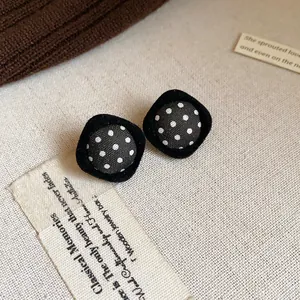 Close-up of retro black velvet square stud earrings with white polka dot fabric detail