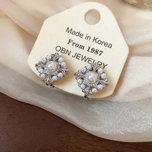 Detailansicht eleganter quadratischer Perlen-Ohrclips mit Iris-Blumendesign aus Metall.