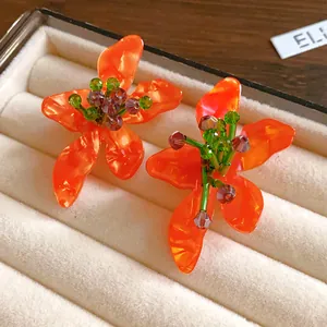 Close-up detail of vibrant orange crystal flower earrings with green accents in a jewelry box
