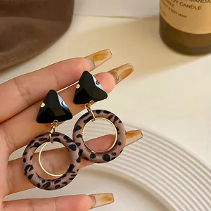 Primer plano de pendientes de aro con estampado de leopardo y pernos negros geométricos.