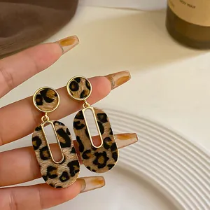 Primer plano de pendientes colgantes con estampado de leopardo y borde de metal dorado.