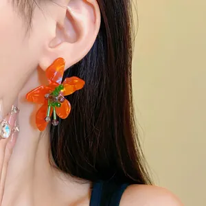 Macro detail of an orange crystal flower earring showing translucent petals and bead work.