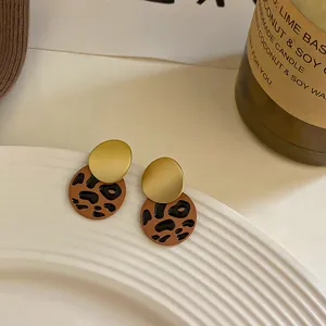 Primer plano de pendientes geométricos con estampado de leopardo y acabado dorado mate.