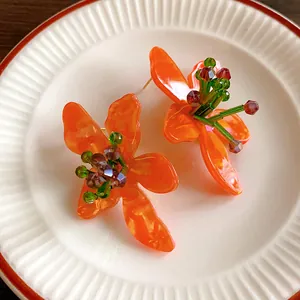 Detail of orange crystal flower stud earrings with silver needles on a white plate