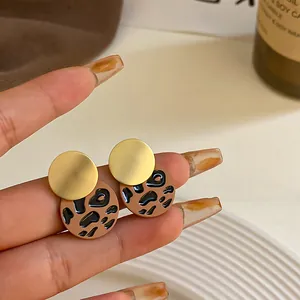 Primer plano detallado de pendientes geométricos de leopardo con acabado dorado mate.
