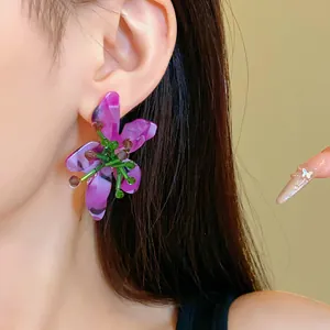 Dettaglio orecchini a fiore in acrilico viola con perle verdi indossati da una modella